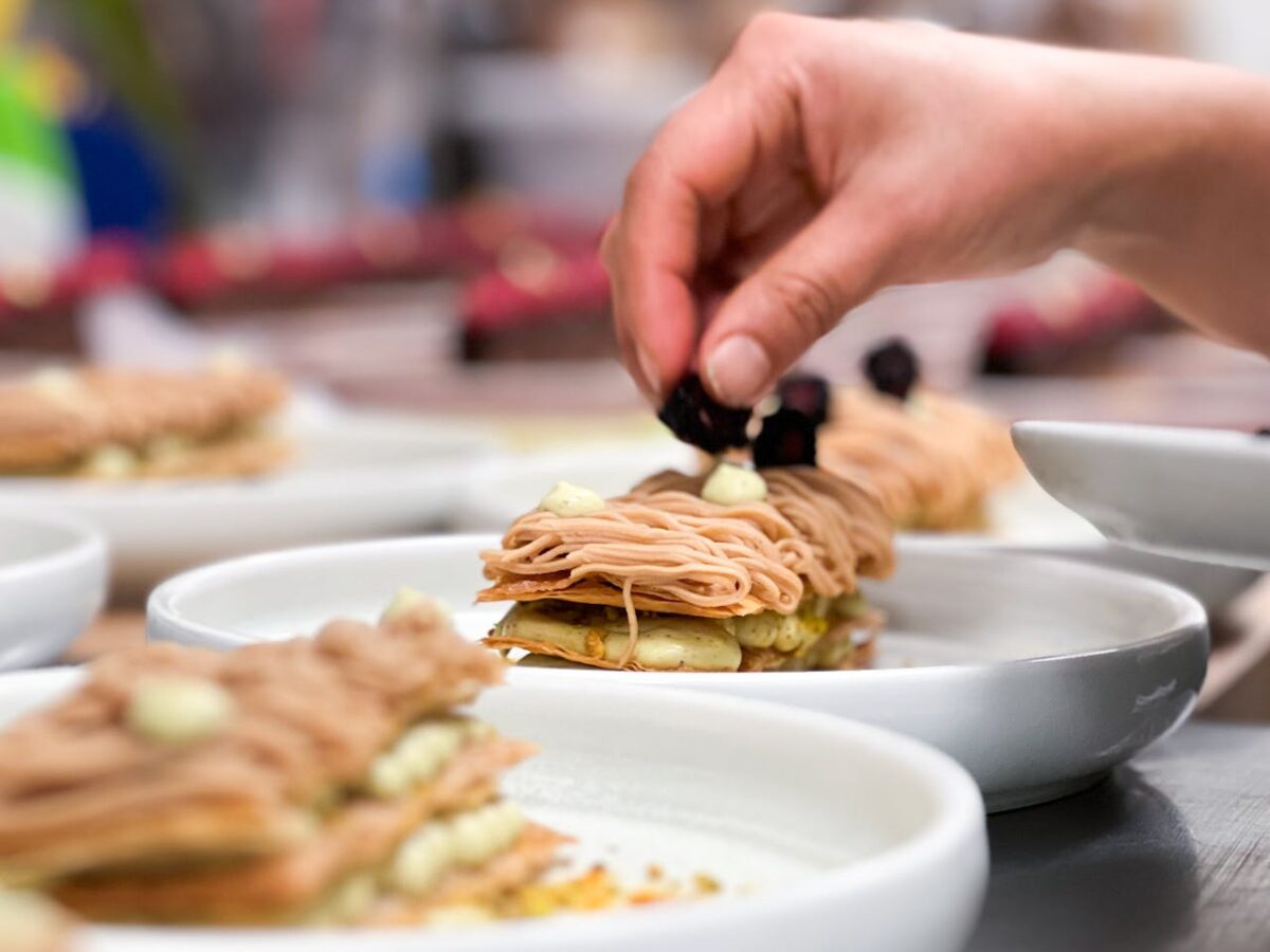 A chef's hand placing garnish on an elegant chestnut dessert in a restaurant.